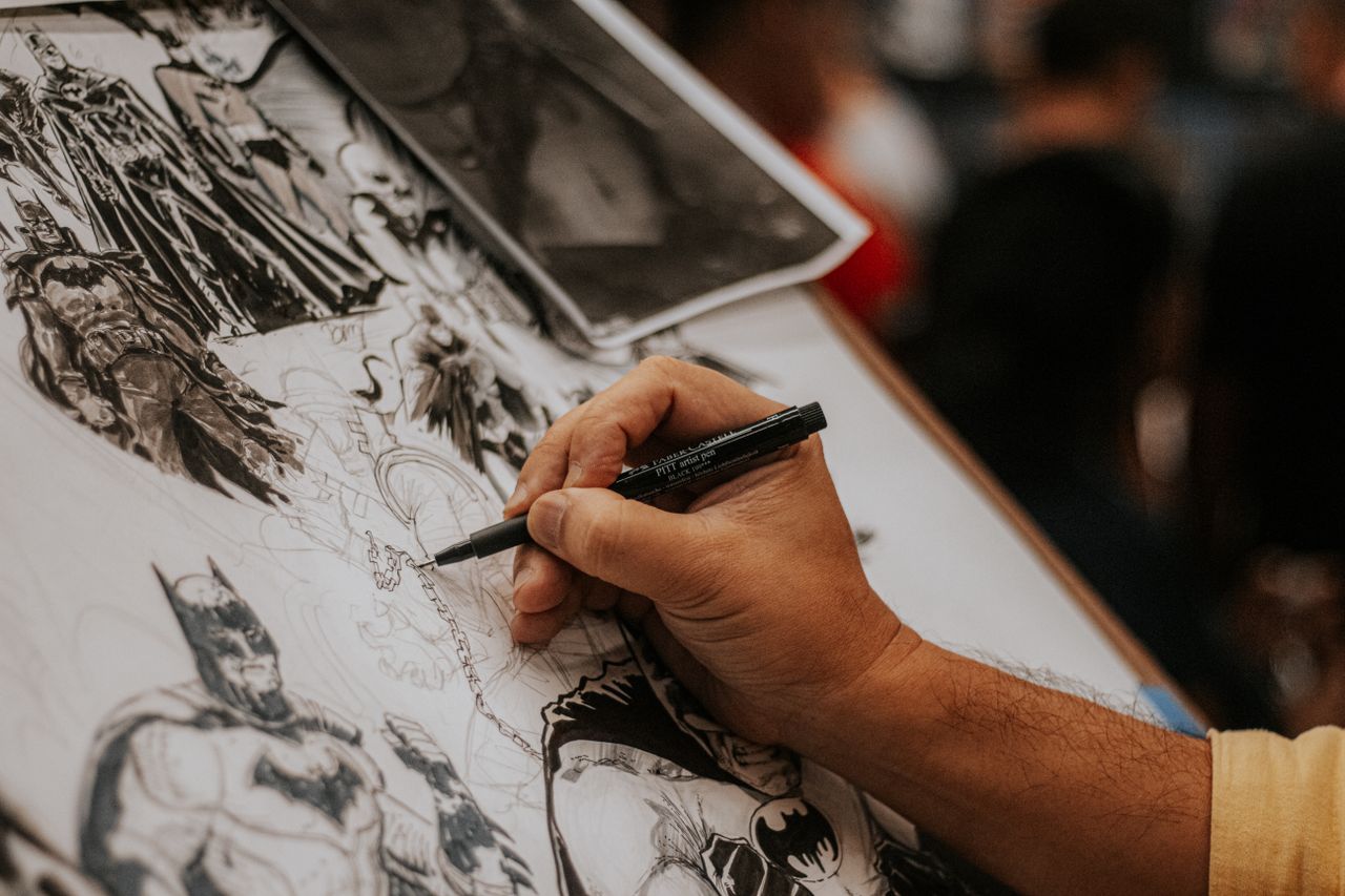 Home Artist drawing detailed comic book characters with a pen at a lively event.