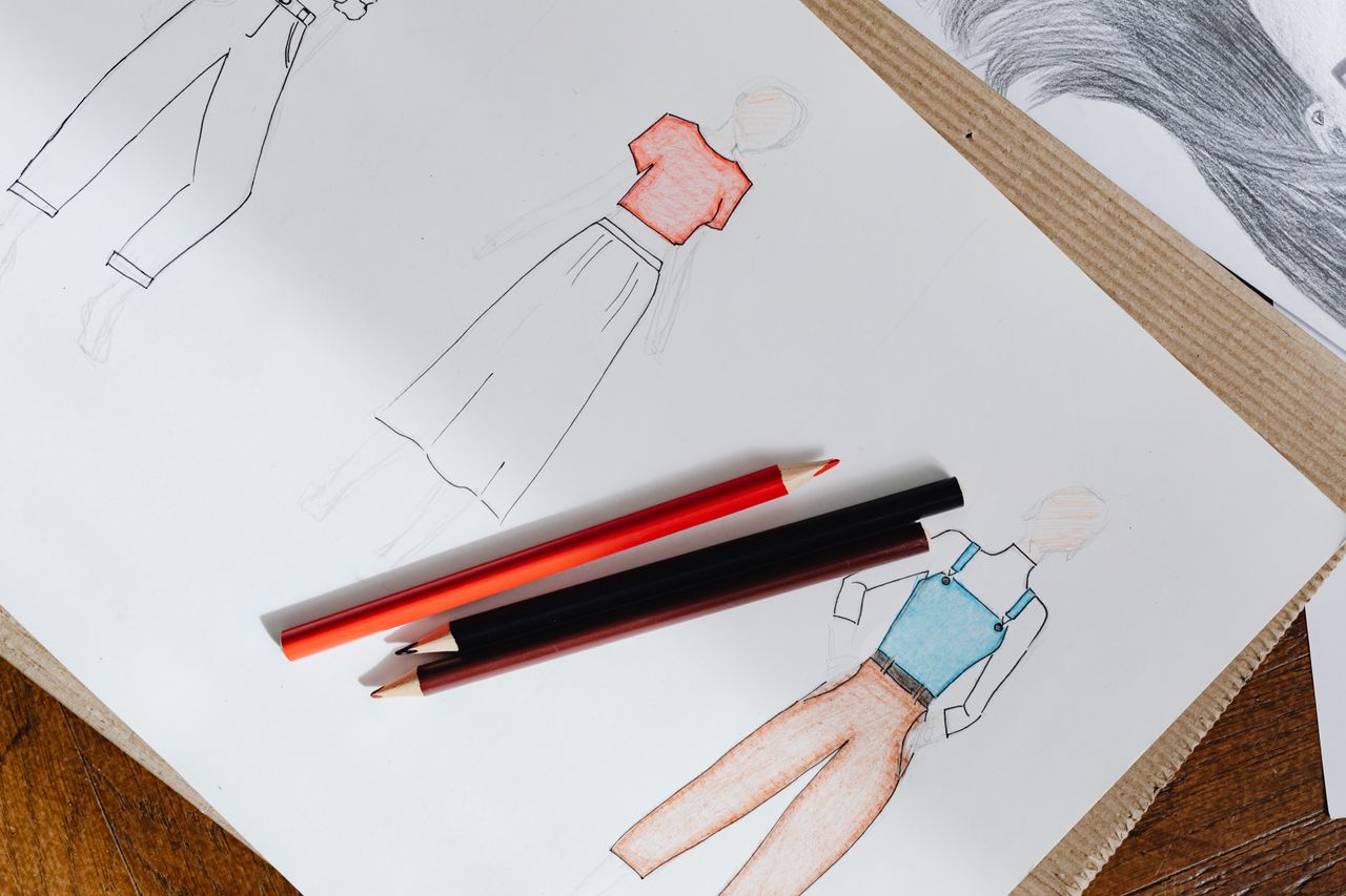 Home Fashion sketches on paper with red and black colored pencils on a wooden surface.